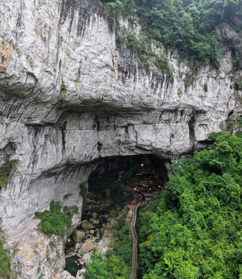 Guiyang China 24 June 2026 Aerial view of the massive limestone cave entrance in Xiuwen County featuring a wooden walkway winding through the lush green forest and rocky terrain.