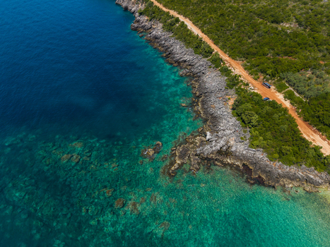 Aerial view of Aquarium Beach featuring a rugged rocky coastline with crystal clear turquoise water and a dirt road through green vegetation in Jala Vlore County Albania. Aerial view of Aquarium Beach featuring a rugged rocky coastline with crystal clear turquoise water and a dirt road through green vegetation in Jala Vlore County Albania.