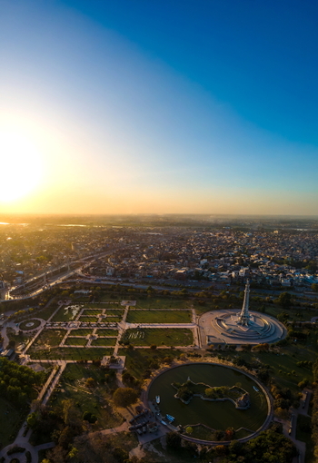 Aerial view of Minar e Pakistan surrounded by lush gardens a circular lake and the sprawling cityscape at sunset in Lahore Punjab Pakistan.