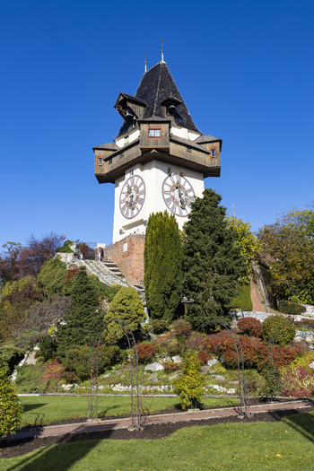 View of the iconic clock tower the Grazer Uhrturm standing tall amidst vibrant autumn foliage under a clear blue sky a beacon of history Graz Styria Austria. View of the iconic clock tower the Grazer Uhrturm standing tall amidst vibrant autumn foliage under a clear blue sky a beacon of history Graz Styria Austria.