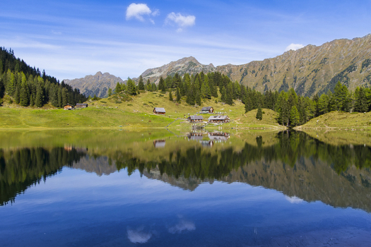View of the glassy Duisitzkarsee lake mirroring the alpine huts nestled against rugged mountains under a bright sky Duisitzkarsee Styria Austria. View of the glassy Duisitzkarsee lake mirroring the alpine huts nestled against rugged mountains under a bright sky Duisitzkarsee Styria Austria.