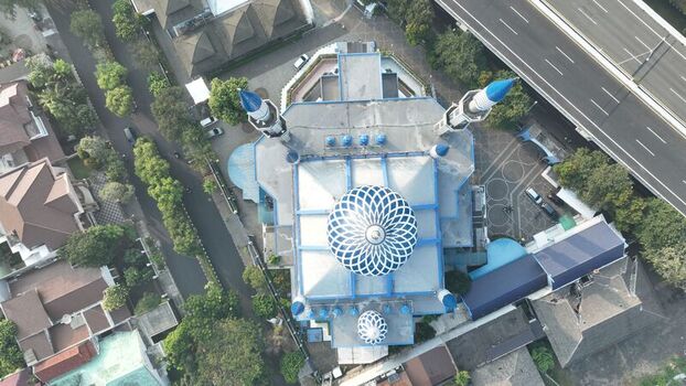 Aerial view of a mosque with a blue geometric dome and minarets surrounded by urban residential buildings and a highway in Bekasi Barat West Java Indonesia. Aerial view of a mosque with a blue geometric dome and minarets surrounded by urban residential buildings and a highway in Bekasi Barat West Java Indonesia.