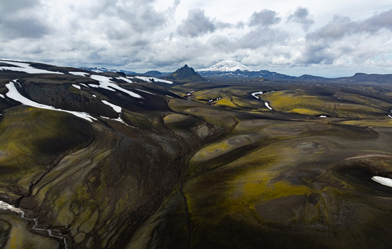 Aerial view of Krakatindur mountain surrounded by mossy volcanic hills dark lava fields and snow patches in Rangarthing ytra Iceland. Aerial view of Krakatindur mountain surrounded by mossy volcanic hills dark lava fields and snow patches in Rangarthing ytra Iceland.