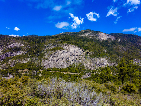 View of the massive granite rock formations and dense evergreen forests under a bright blue sky in Yosemite National Park California United States. View of the massive granite rock formations and dense evergreen forests under a bright blue sky in Yosemite National Park California United States.