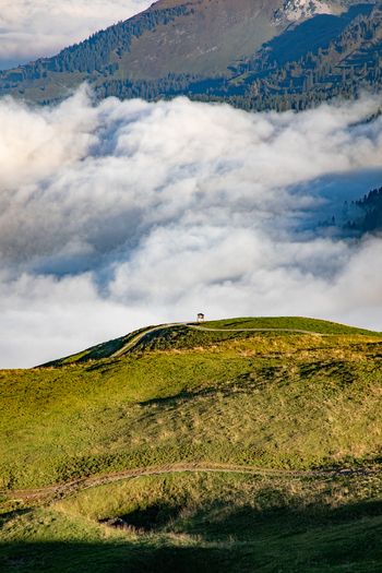 Aerial view of a small structure perched on a grassy mountain ridge above a sea of clouds in the Swiss Alps Airolo Ticino Switzerland. Aerial view of a small structure perched on a grassy mountain ridge above a sea of clouds in the Swiss Alps Airolo Ticino Switzerland.