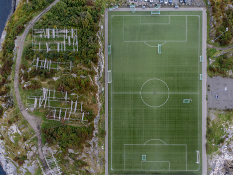 Aerial view of a vibrant green sports field contrasts sharply with the rugged rocky terrain that surrounds it Molde Norway. Aerial view of a vibrant green sports field contrasts sharply with the rugged rocky terrain that surrounds it Molde Norway.