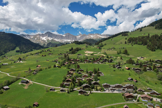 Aerial view of traditional wooden chalets nestled among green alpine pastures and snow capped mountains Rougemont Vaud Switzerland. Aerial view of traditional wooden chalets nestled among green alpine pastures and snow capped mountains Rougemont Vaud Switzerland.