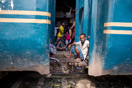 Dhaka Bangladesh 14 June 2018 View of a man sitting on the coupling between two blue train cars at Airport Railway Station with passengers moving in the background. Dhaka Bangladesh 14 June 2018 View of a man sitting on the coupling between two blue train cars at Airport Railway Station with passengers moving in the background.