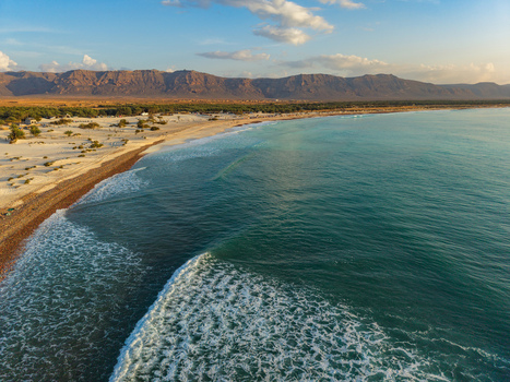 Aerial view of turquoise waves caress the sandy beach meeting the arid landscape under a vast sky Kadrihnitin Socotra Yemen. Aerial view of turquoise waves caress the sandy beach meeting the arid landscape under a vast sky Kadrihnitin Socotra Yemen.