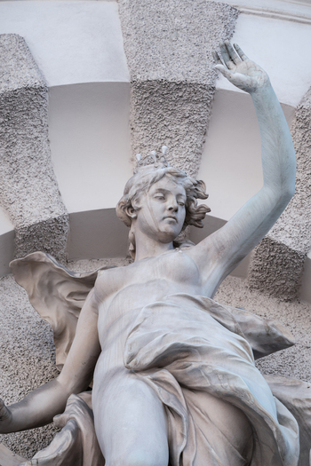 View of a classical stone sculpture of a woman with a raised arm and crown on a historic building facade in Vienna Austria. View of a classical stone sculpture of a woman with a raised arm and crown on a historic building facade in Vienna Austria.