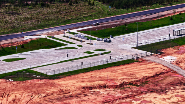 Aerial view of a newly constructed parking lot with paved spaces adjacent to a road and surrounded by cleared earth and green grass in Latvija. Aerial view of a newly constructed parking lot with paved spaces adjacent to a road and surrounded by cleared earth and green grass in Latvija.