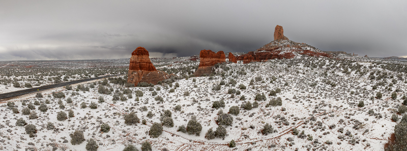 Aerial view of snow covered red rock buttes and desert landscape under a dramatic overcast sky near a winding road in Page Arizona United States.