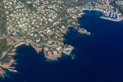 Aerial view of Le Trayas featuring luxury villas nestled among red rocky cliffs a marina with boats and the deep blue Mediterranean Sea in Saint Raphael Provence Alpes Cote d Azur France. Aerial view of Le Trayas featuring luxury villas nestled among red rocky cliffs a marina with boats and the deep blue Mediterranean Sea in Saint Raphael Provence Alpes Cote d Azur France.