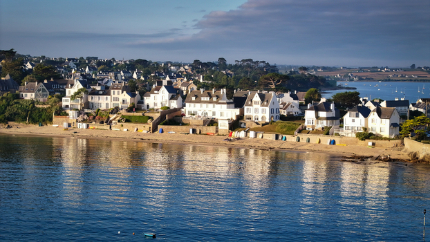 Aerial view of sunlight kissing the tranquil waters as it meets the sandy beach and the quaint white roofed houses of Carantec Brittany France. Aerial view of sunlight kissing the tranquil waters as it meets the sandy beach and the quaint white roofed houses of Carantec Brittany France.