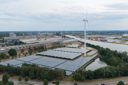 Aerial view of the Haven Genk solar power plant featuring extensive photovoltaic panels a wind turbine and industrial infrastructure along an inland waterway in Genk Vlaanderen Belgium.
