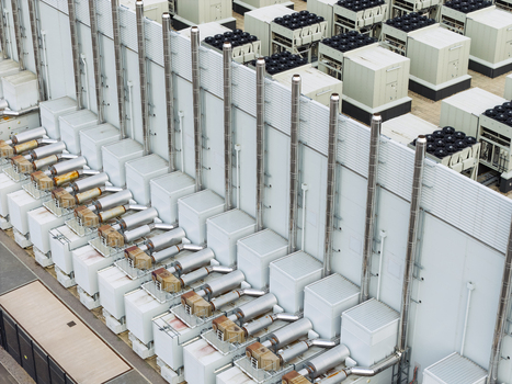 Aerial view of a data center featuring rows of industrial cooling units and ventilation pipes on a flat roof in the United Kingdom.