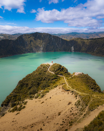 Aerial view of Quilotoa Lake with its turquoise water surrounded by volcanic crater walls and a person standing on a ridge in Quilotoa Cotopaxi Ecuador. Aerial view of Quilotoa Lake with its turquoise water surrounded by volcanic crater walls and a person standing on a ridge in Quilotoa Cotopaxi Ecuador.