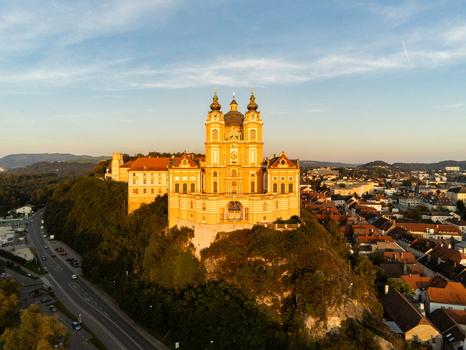 Aerial view of Melk Abbey a historic Benedictine abbey perched on a rocky outcrop overlooking the town of Melk surrounded by lush greenery and urban rooftops in Melk Niederosterreich Austria. Aerial view of Melk Abbey a historic Benedictine abbey perched on a rocky outcrop overlooking the town of Melk surrounded by lush greenery and urban rooftops in Melk Niederosterreich Austria.