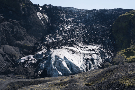 View of the Eyjafjallajokull glacier surrounded by rugged black volcanic rock and mossy slopes in Hvolsvollur Rangarthing eystra Iceland. View of the Eyjafjallajokull glacier surrounded by rugged black volcanic rock and mossy slopes in Hvolsvollur Rangarthing eystra Iceland.