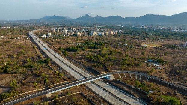 Aerial view of the JNPT highway infrastructure near Badlapur featuring a concrete overpass dry landscape and distant buildings against hills in Badlapur Maharashtra India. Aerial view of the JNPT highway infrastructure near Badlapur featuring a concrete overpass dry landscape and distant buildings against hills in Badlapur Maharashtra India.