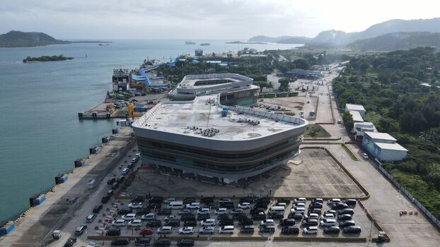 Aerial view of the modern terminal building at Bakauheni Port with a large parking area coastal waters and lush green hills in Bakauheni Lampung Indonesia.