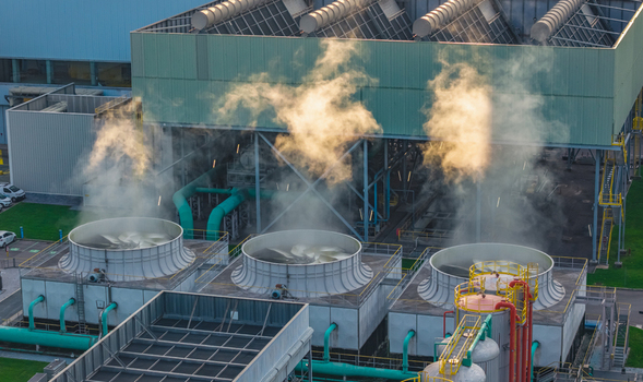 Aerial view of cooling towers and heavy industrial infrastructure releasing steam at a large manufacturing and metal processing facility in Brescia Lombardy Italy.