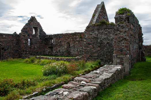 View of the historic stone ruins of Iona Nunnery with weathered walls and green grass under a cloudy sky in Baile Mor Scotland United Kingdom. View of the historic stone ruins of Iona Nunnery with weathered walls and green grass under a cloudy sky in Baile Mor Scotland United Kingdom.