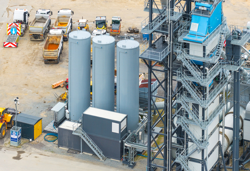 Aerial view of an asphalt mixing plant with large grey silos industrial structures and parked dump trucks in Pomeranian Voivodeship Poland.