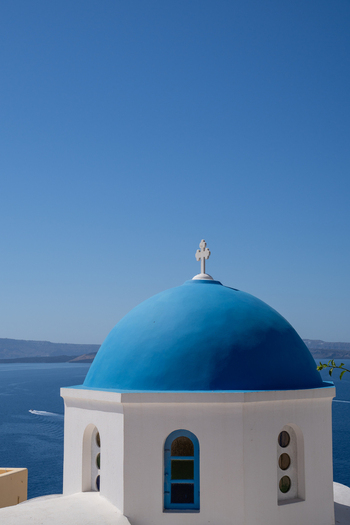 View of a traditional white church with a bright blue dome and a small cross overlooking the deep blue Aegean Sea under a clear sky in Fira Greece. View of a traditional white church with a bright blue dome and a small cross overlooking the deep blue Aegean Sea under a clear sky in Fira Greece.
