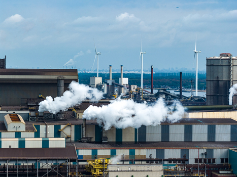 Aerial view of the Tata Steel plant with industrial buildings smoke stacks emitting steam and wind turbines in the background in Velsen Noord Noord Holland Netherlands. Aerial view of the Tata Steel plant with industrial buildings smoke stacks emitting steam and wind turbines in the background in Velsen Noord Noord Holland Netherlands.