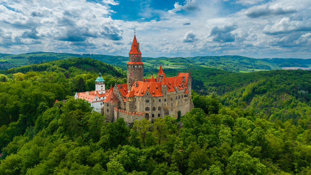 Aerial view of Bouzov Castle with its red tiled roofs and tall spire surrounded by lush green forests Bouzov Olomoucky kraj Czechia. Aerial view of Bouzov Castle with its red tiled roofs and tall spire surrounded by lush green forests Bouzov Olomoucky kraj Czechia.