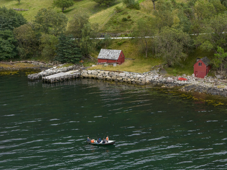 Aerial view of Hardangerfjord with fishermen in a small boat near traditional red wooden cabins and a stone pier in Blurnes Vestland Norway. Aerial view of Hardangerfjord with fishermen in a small boat near traditional red wooden cabins and a stone pier in Blurnes Vestland Norway.