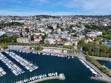 Aerial view of the Ouchy Olympique marina with numerous sailboats docked in the harbor lined by a tree shaded promenade and urban architecture in Lausanne Vaud Switzerland. Aerial view of the Ouchy Olympique marina with numerous sailboats docked in the harbor lined by a tree shaded promenade and urban architecture in Lausanne Vaud Switzerland.