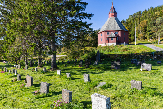 View of Hadsel Church a red octagonal wooden building with a graveyard and headstones on a green lawn under a clear blue sky in Stokmarknes Nordland Norway. View of Hadsel Church a red octagonal wooden building with a graveyard and headstones on a green lawn under a clear blue sky in Stokmarknes Nordland Norway.