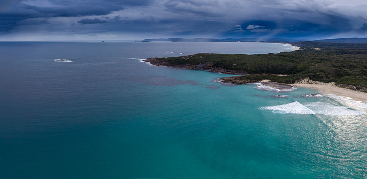 Aerial view of Conspicuous Cliff and the rugged coastline with turquoise waters sandy beach and dark stormy clouds overhead in Nornalup Western Australia Australia. Aerial view of Conspicuous Cliff and the rugged coastline with turquoise waters sandy beach and dark stormy clouds overhead in Nornalup Western Australia Australia.