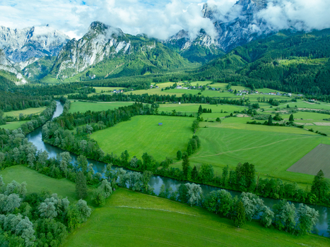 Aerial view of Nationalpark Gesause with the Enns river winding through lush green meadows and dense forests under dramatic mountain peaks in Admont Steiermark Austria.