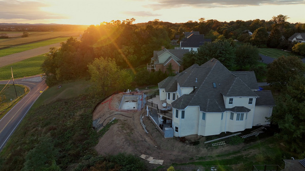 Aerial view of a residential house with a swimming pool under construction surrounded by autumn trees and fields at sunset in Rothsville Pennsylvania United States.