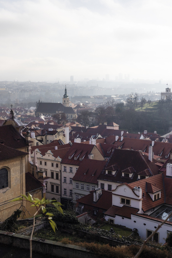 View of red tiled rooftops and historic church spires under a misty overcast sky in Prague Prague Czechia. View of red tiled rooftops and historic church spires under a misty overcast sky in Prague Prague Czechia.