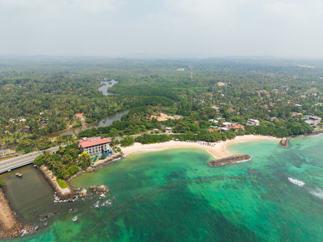Aerial view of Devil s Rock formation in turquoise waters near a sandy beach and lush palm forests Ahangama Southern Province Sri Lanka. Aerial view of Devil s Rock formation in turquoise waters near a sandy beach and lush palm forests Ahangama Southern Province Sri Lanka.