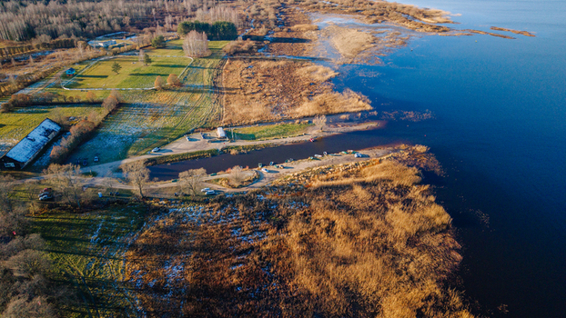 Aerial view of Lake Burtnieks coastline featuring golden reed beds rural fields with light frost and small boats moored along the shore in Burtnieki Valmiera Municipality Latvia.