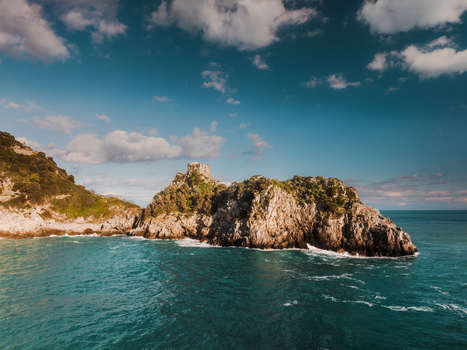 Aerial view of a rugged rocky island rising dramatically from the turquoise sea under a sky dotted with fluffy clouds Amalfi Campania Italy. Aerial view of a rugged rocky island rising dramatically from the turquoise sea under a sky dotted with fluffy clouds Amalfi Campania Italy.