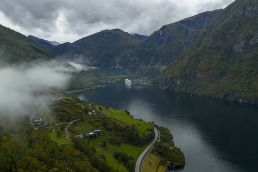 Aerial view of the Aurlandsfjord with a cruise ship docked at the village of Flam surrounded by steep mountains and low clouds in Flam Vestland Norway.