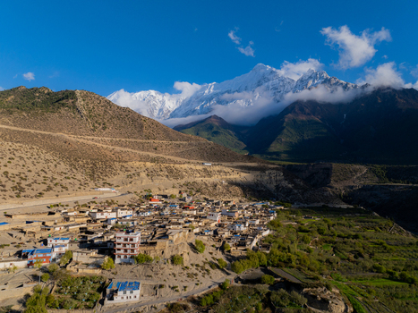 Aerial view of a traditional village nestled in the rugged Himalayan mountains with stone houses terraced fields and snow capped peaks in Nepal.
