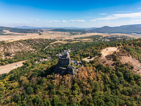 Aerial view of Holloko Castle on a wooded hill above farmland and the village of Holloko Hungary with rolling forested hills in late summer countryside. Aerial view of Holloko Castle on a wooded hill above farmland and the village of Holloko Hungary with rolling forested hills in late summer countryside.