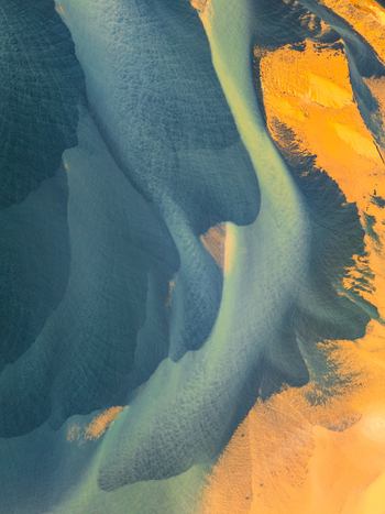 Aerial view of a glacial river delta in Iceland featuring intricate patterns of blue water dark sediment and golden yellow sand banks Iceland. Aerial view of a glacial river delta in Iceland featuring intricate patterns of blue water dark sediment and golden yellow sand banks Iceland.