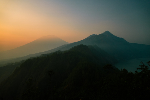 View of Mount Batur and surrounding volcanic landscape at sunrise with silhouettes of mountain ridges and a glimpse of the lake in Kintamani Bali Indonesia.