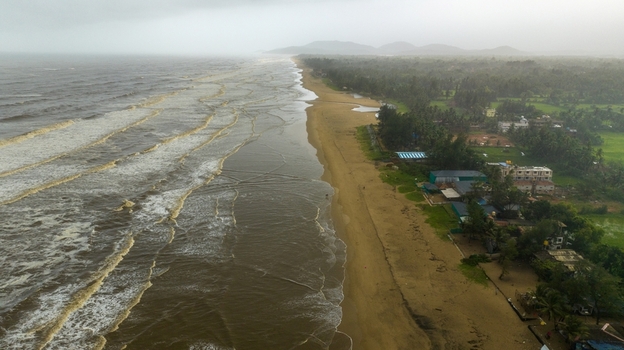 Aerial view of Gokarna beach with dark storm clouds over the coastline crashing waves and lush green vegetation along the shore in Gokarna Karnataka India.