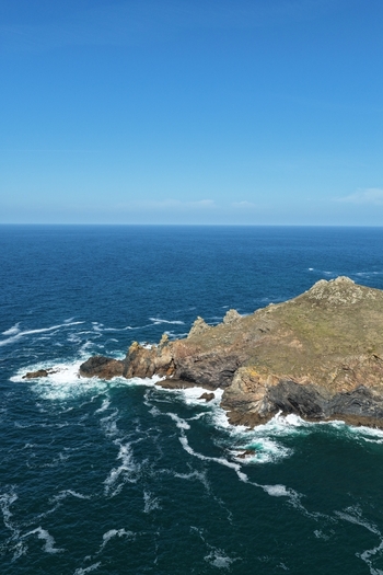 Aerial view of The Rumps coastal headland with rugged cliffs crashing waves and deep blue sea under a clear sky in Wadebridge England United Kingdom. Aerial view of The Rumps coastal headland with rugged cliffs crashing waves and deep blue sea under a clear sky in Wadebridge England United Kingdom.