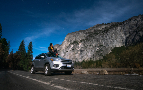 View of a person sitting on the roof of a silver SUV parked on a road beneath the granite cliffs of El Capitan in Yosemite National Park United States of America. View of a person sitting on the roof of a silver SUV parked on a road beneath the granite cliffs of El Capitan in Yosemite National Park United States of America.