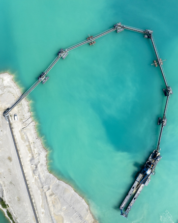 Aerial view of a gravel extraction site with a long conveyor belt system extending into a turquoise water reservoir in Aschheim Bavaria Germany.